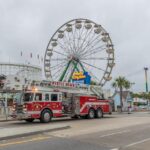 The fire truck in front of a ferris wheel.