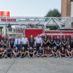 The riders and other fire-fighters in front of a fire truck.