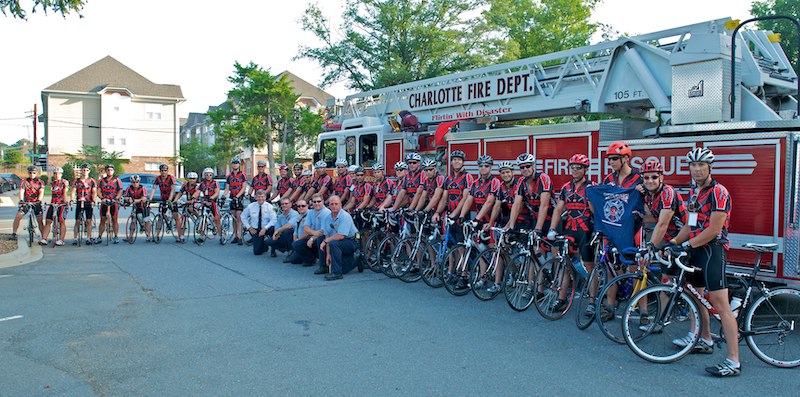 Firefighters and riders in front of a fire truck.